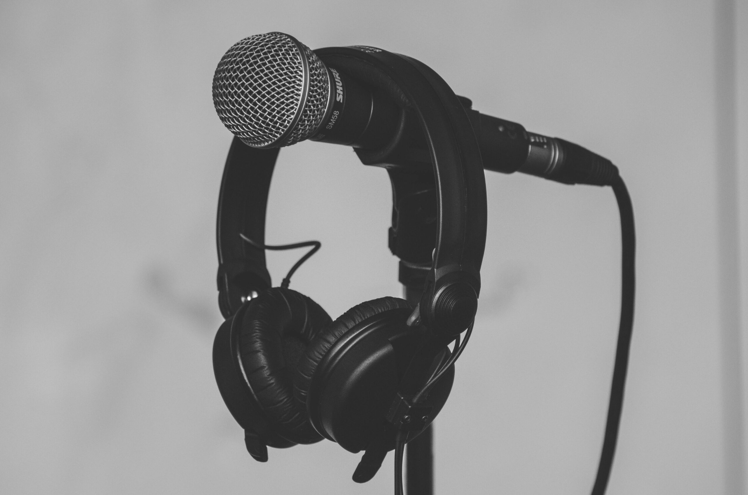 black and white image of a pair of headphones dangling from a microphone on a stand