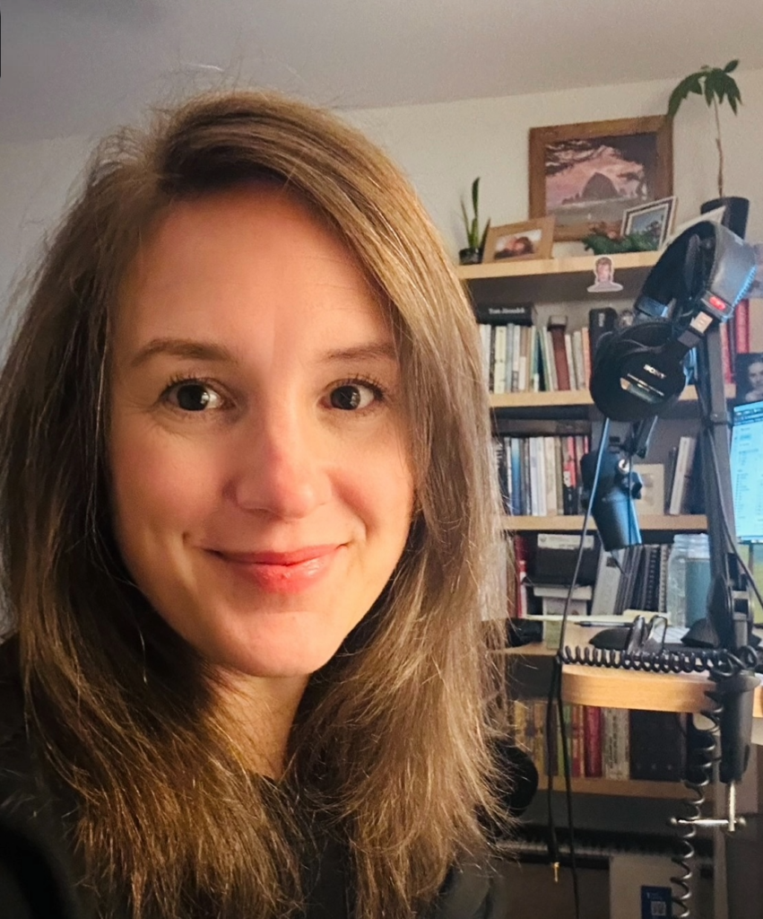 Harmony Jiroudek smiling at the camera with a microphone and bookcase behind her